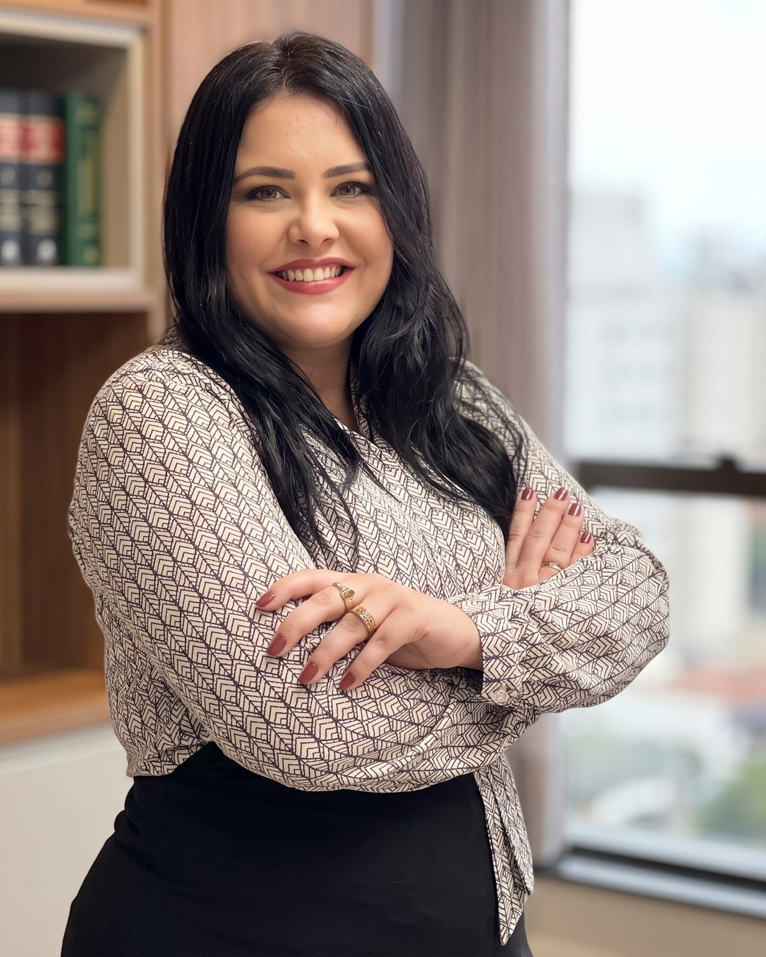Retrato de Juliana Losnake, advogada, de braços cruzados em seu escritório